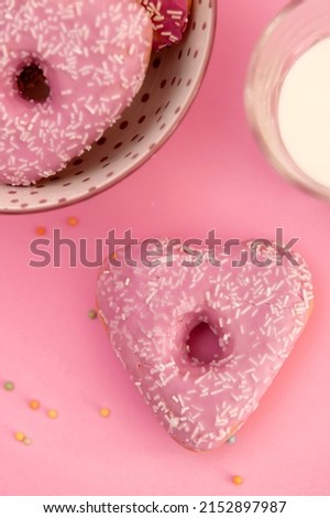 Pink heart shaped donut on a pink table with a glass of milk flat lay picture