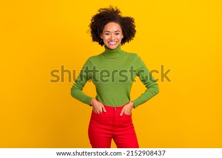 Portrait of attractive cheerful wavy-haired girl holding hands in pockets isolated over bright yellow color background