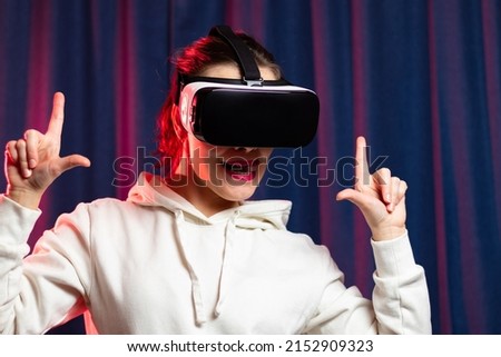 A beautiful young woman in virtual reality glasses plays video games and a white hoodie on a purple background. Modern technologies. Selective focus. Close-up. Portrait