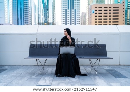 Arab businesswoman working on laptop sitting outdoor. Muslim Saudi Arabian woman in a meeting wearing Abaya and Hijab in business background