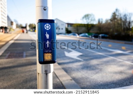 Pedestrian signal button with an orange light indicating that it is not possible to cross with the road in the background.