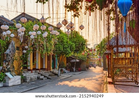 Awesome view of cozy street decorated with colorful silk lanterns at sunrise. Scenic traditional old yellow houses of Hoi An Ancient Town, Vietnam. Hoian is a popular tourist destination of Asia. Royalty-Free Stock Photo #2152940249