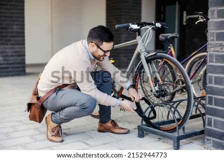 A smiling urban businessman locking up a bike on the street.