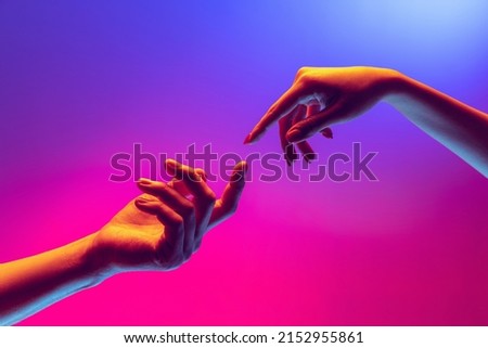 Moment of weightless. Two human hands trying to touch each other isolated on purple background in neon light. Concept of human relation, community, togetherness, symbolism, culture and history