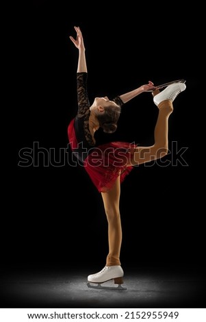 Upright spin. Studio shot of little female figure skater in beautiful stage attire skating isolated on black background in spotlight. Concept of movement, sport, beauty. Copy space for ad, text