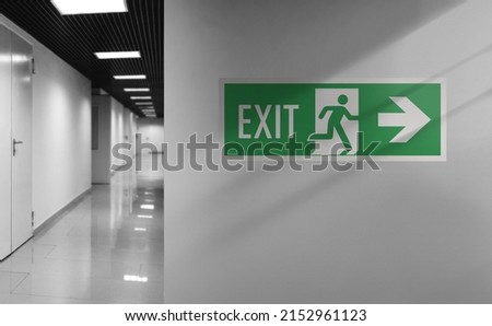 Emergency exit sign. Interior internal corridor of modern office. Corridor with light walls, black ceiling and shiny floor. Soft focus. Royalty-Free Stock Photo #2152961123