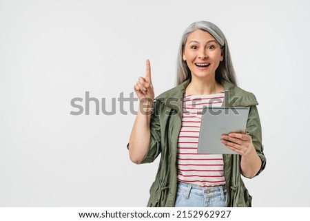 Smart caucasian mature middle-aged woman grandmother holding digital tablet pointing upwards on idea copy space, using mobile application for social media, e-banking, e-commerce isolated in white