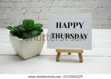 Happy Thursday text on wooden easel standing on white brick wall and wooden background
