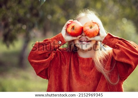 portrait of girl eating red organic apple outdoor. Harvest Concept. Child picking apples on farm in autumn. Children and Ecology. Healthy nutrition Garden Food. Girl holding in front of her face apple Royalty-Free Stock Photo #2152969345