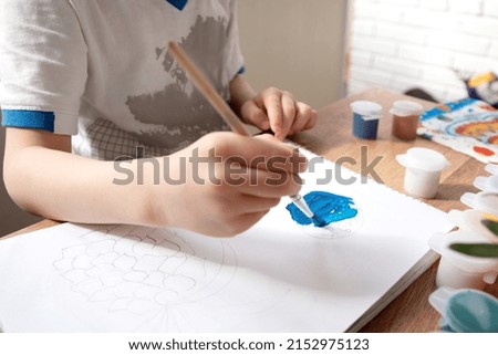 Kid drawing with blue gouache paint in album close up
