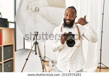 African american photographer man working at photography studio smiling doing phone gesture with hand and fingers like talking on the telephone. communicating concepts. 