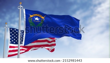 The Nevada state flag waving along with the national flag of the United States of America. In the background there is a clear sky. Nevada is a state in the Western region of the United States Royalty-Free Stock Photo #2152981443