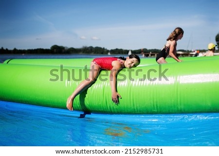 Children play on the water slide in the open air, the girl is resting after playing in the water by the lake in full sun