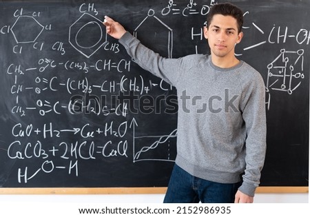 the teacher writes on the blackboard various formulas for chemistry in high school. a young Arab teacher points his finger at the formulas. Back to school concept