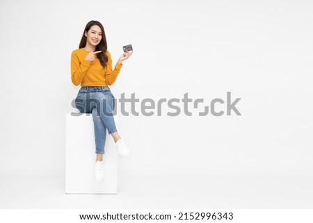 Happy young Asian woman sitting and pointing to credit card for paying online business isolated on white background Royalty-Free Stock Photo #2152996343