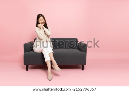 Excited Asian businesswoman sitting on sofa isolated on pink background