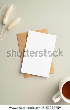 Top view vertical photo of paper card craft paper envelope cup of tea and white lagurus flowers on pastel grey background with empty space