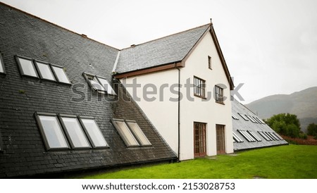 A beautiful exterior shot of a wet modern stone building walls with glass windows on grass land against a light sky