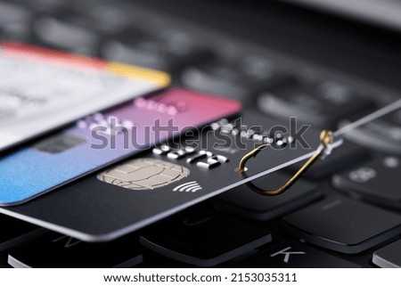 Credit card phishing scam concept. Credit card data theft, card hooked on fishing hook pulled from stack of other cards on keyboard. Royalty-Free Stock Photo #2153035311
