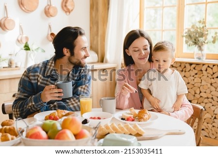 Morning breakfast at home. Young caucasian family of three, parents and infant toddler new born baby eating together, feeding son daughter at home kitchen. Parenthood concept Royalty-Free Stock Photo #2153035411
