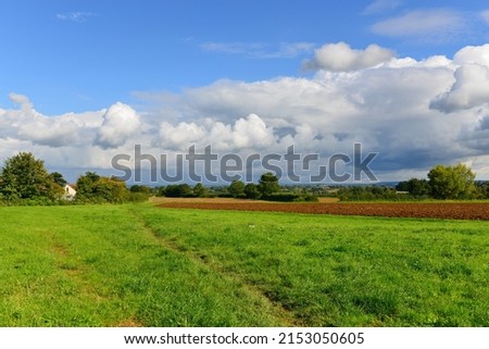 Scenic farmland view of a green field with ploughed earth in the distance and a beautiful cloudy sky above Royalty-Free Stock Photo #2153050605