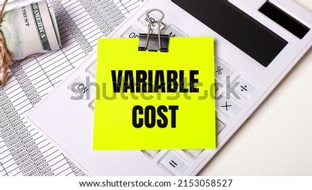 On a light background - cash, a white calculator and a yellow sticker under a black paper clip with the text VARIABLE COST. Business concept