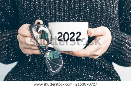 Female hands hold glasses and a white sheet of paper with the inscription 2022