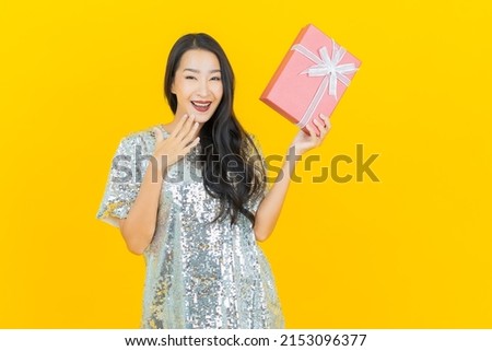 Portrait beautiful young asian woman smile with red gift box on yellow color background