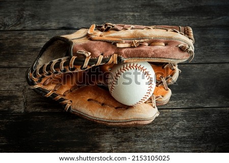 Leather baseball or softball glove with ball on rustic wooden background.