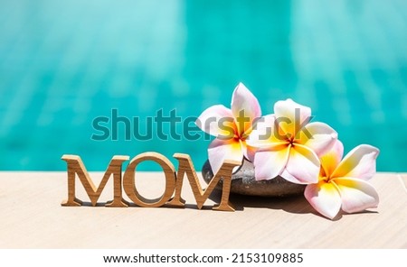 Happy Mother's day in tropical concept, mom wooden alphabet with plumeria flower over blue water background
