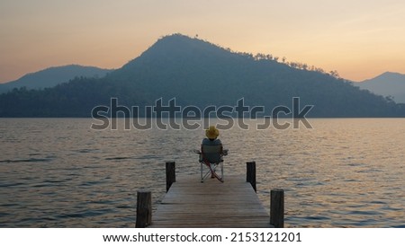 Asia people woman enjoy sit calm day dream on cozy chair at river pier hand behind head. Wide view of cloud dawn dusk sky solo budget staycation getaway at glamping take city life break stress relief. Royalty-Free Stock Photo #2153121201