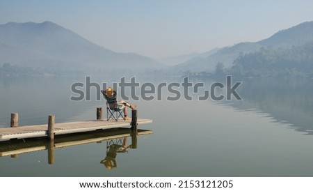 Asia people woman enjoy sit calm day dream on cozy chair at river pier hand behind head. Wide view of cloud dawn dusk sky solo budget staycation getaway at glamping take city life break stress relief. Royalty-Free Stock Photo #2153121205