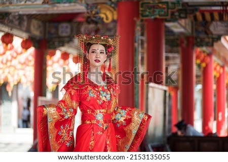 portrait of a woman. person in traditional costume. woman in traditional costume. Beautiful young woman in a bright red dress and a crown of Chinese Queen posing against the ancient door.  Royalty-Free Stock Photo #2153135055