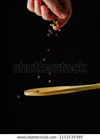 Seasonings, spices in a frozen flight fall on a wooden spoon on a black background. Minimalism. There are no people in the photo. Ingredient for meals. Restaurant, hotel, advertising, banner.