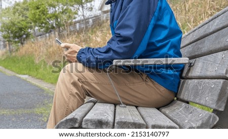 A man sitting on a park bench. He uses a smartphone.