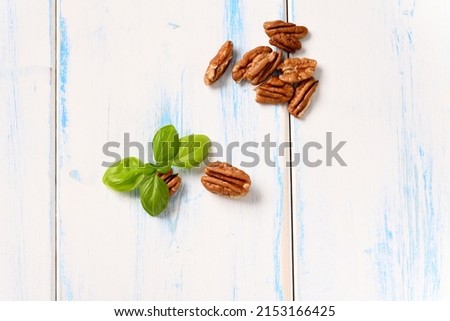 Pecans with basil leaf on a light wooden table.