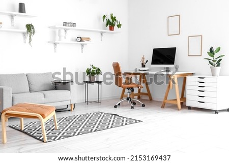 Comfortable sofa and workplace with modern computer near white wall in room interior Royalty-Free Stock Photo #2153169437