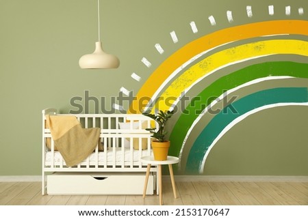 Crib near green wall with painted rainbow in children's room