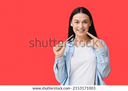 Beautiful woman with toothbrush pointing at dental braces on red background