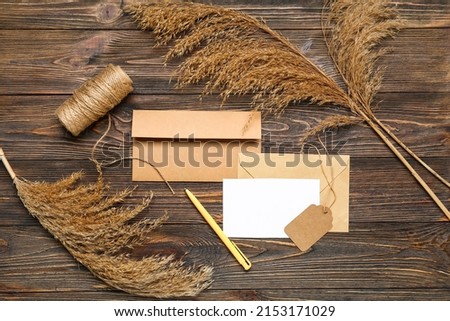 Envelopes with blank card, tag, pen and pampas grass on dark wooden background