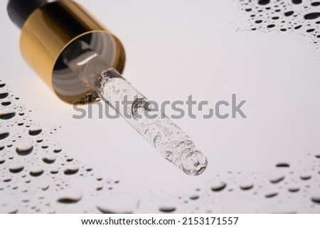 A pipette of cosmetic gel on the background of drops.