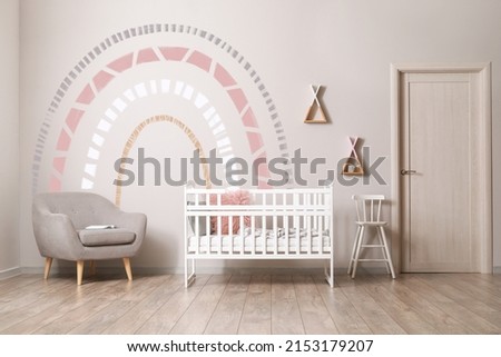 Interior of children's room with crib, armchair and light wall with painted rainbow