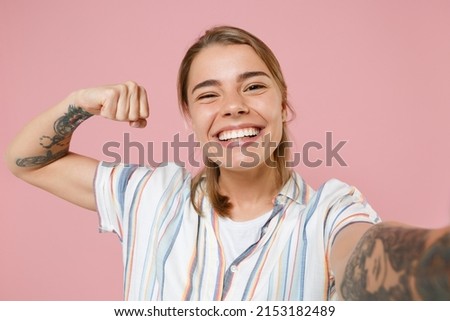 Close up of smiling young blonde woman girl in casual striped shirt isolated on pink background. People lifestyle concept. Mock up copy space. Doing selfie shot on mobile phone showing biceps muscles