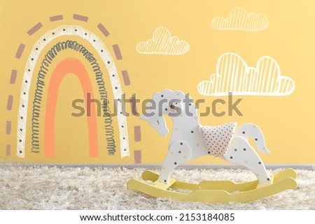Rocking horse near color wall with painted rainbow in children's room