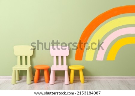 Small chairs, stools and wall with painted rainbow in children's room