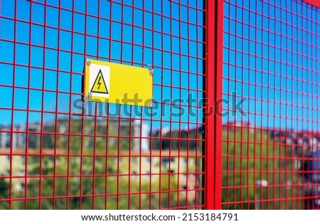High voltage warning sign hanging from the red grille