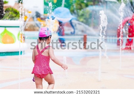 Rear black view. Portrait of 3-4 years old. Asian child girl playing courtyard fountain. In summer time. Kid wearing red swimming suit. Brightness in childhood. Activities with hot weather. Copy space