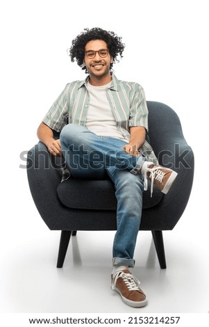people and furniture concept - happy smiling young man in glasses sitting in chair over white background
