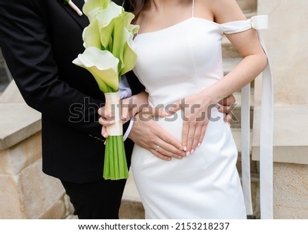 Beautiful young couple of brides posing making hands a heart on the belly of a pregnant bride. High quality photo