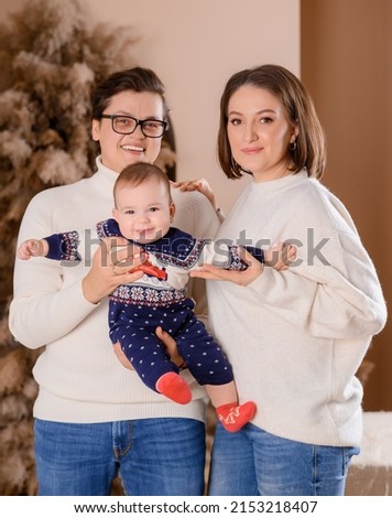 Young family dad mom son toddler on the background of Christmas tree decor in beige tones in winter clothes. High quality photo